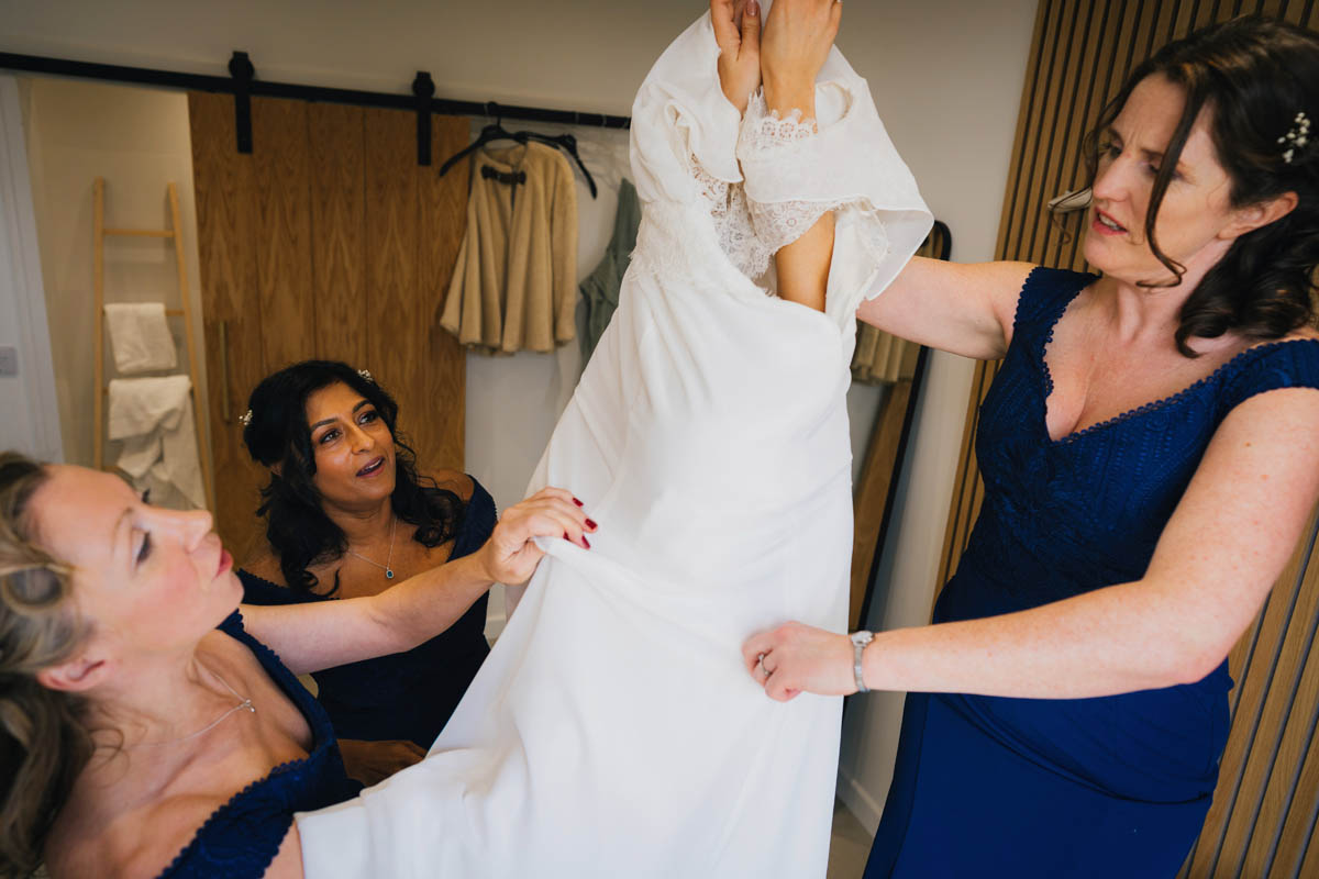 three bridesmaids in navy dresses help pull the bride's dress over her shoulders