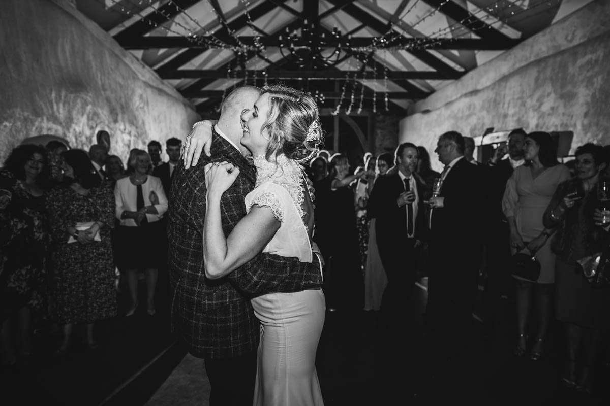 the newly married d couple throw their arms around each other on the dance floor, monochrome photograph at Upton Barn