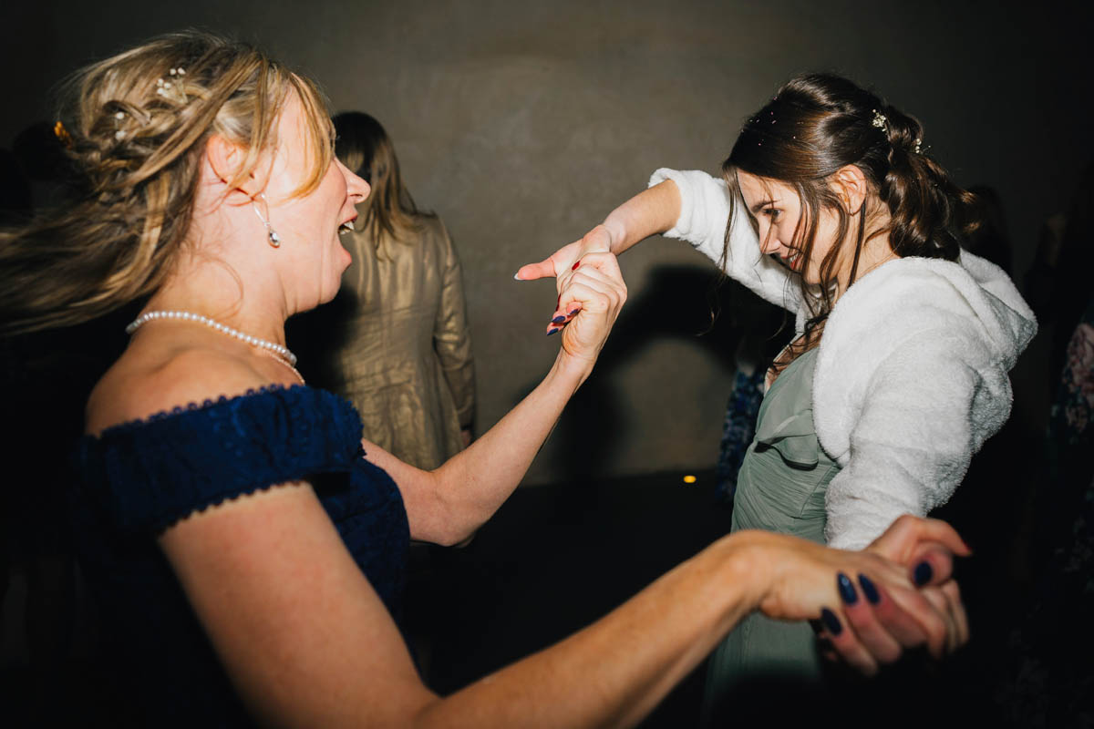 a woman dances with her friend's teenage daughter on the dance floor at the wedding