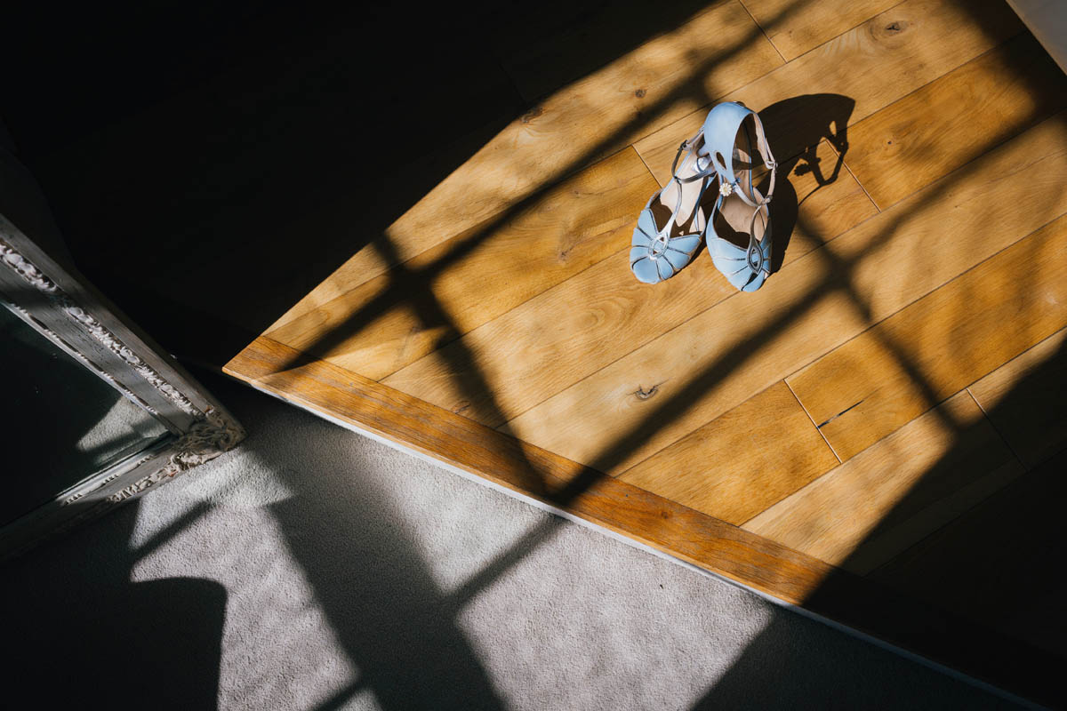 bride's blue high heeled shoes in the window light. The window frame casts shadows and highlights across the floor