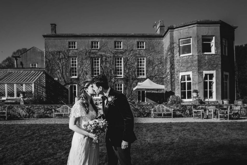black and white photograph of the newly married couple kissing in front of pennard house