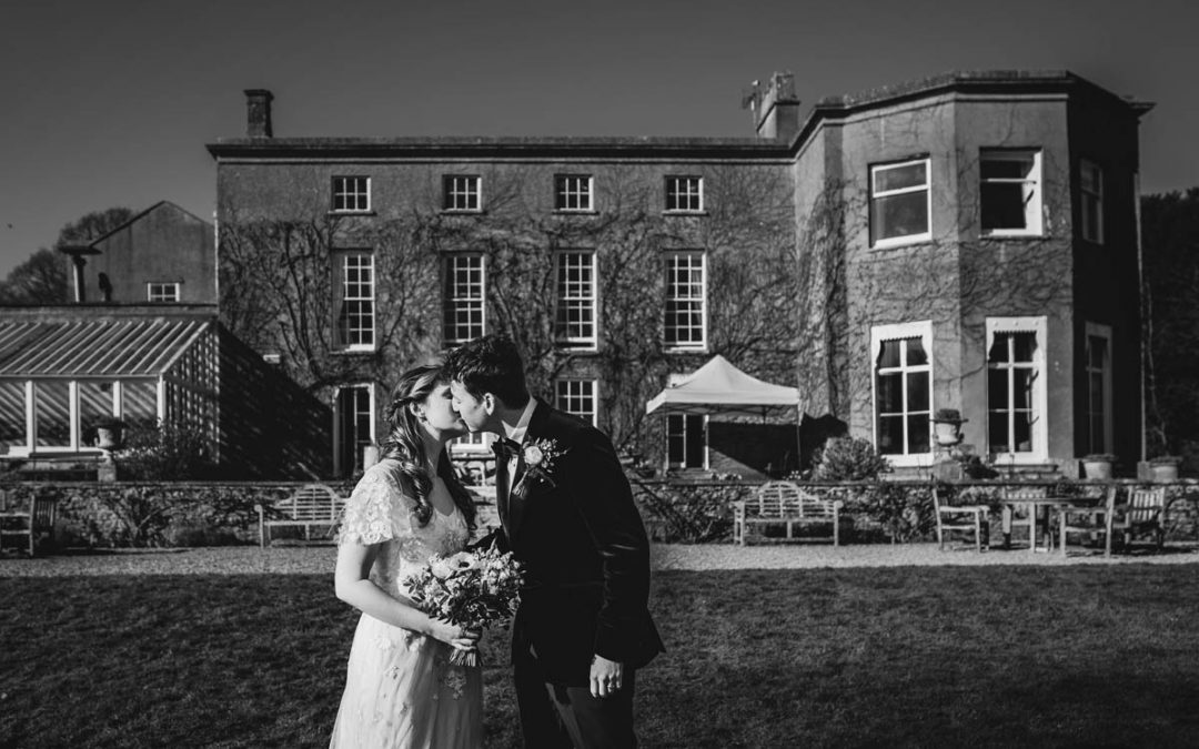 black and white photograph of the newly married couple kissing in front of pennard house
