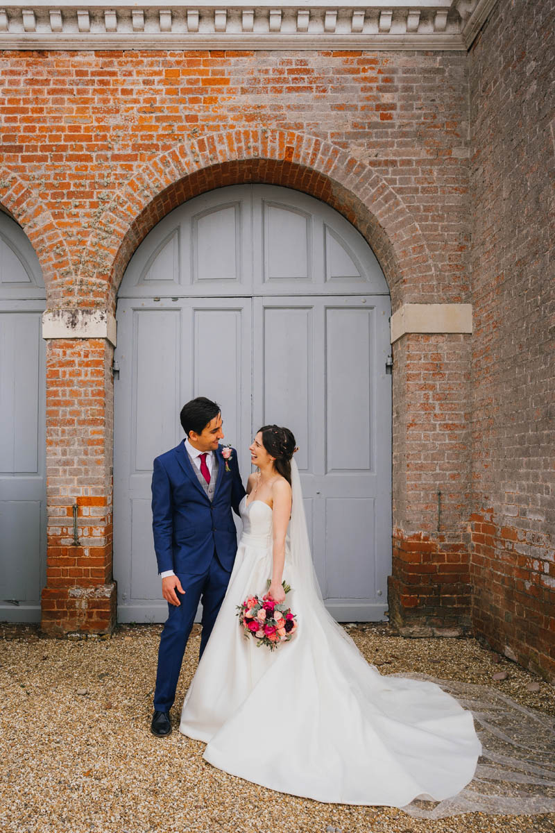 the groom and bride look at one another and laugh in front of the barn doors at rockbeare manor