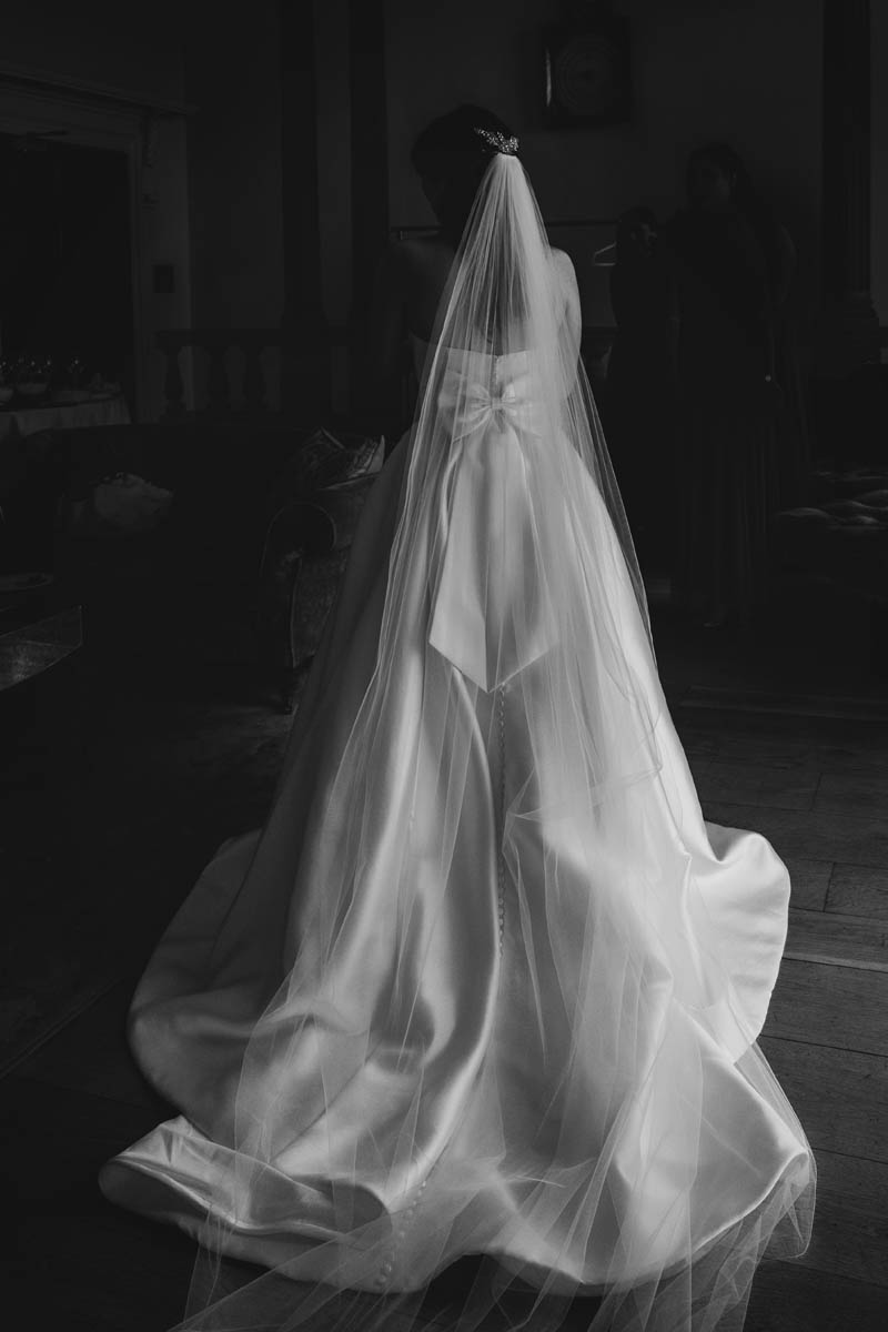 black and white photograph of the bride in window light. the light catches her veil and wedding Dres