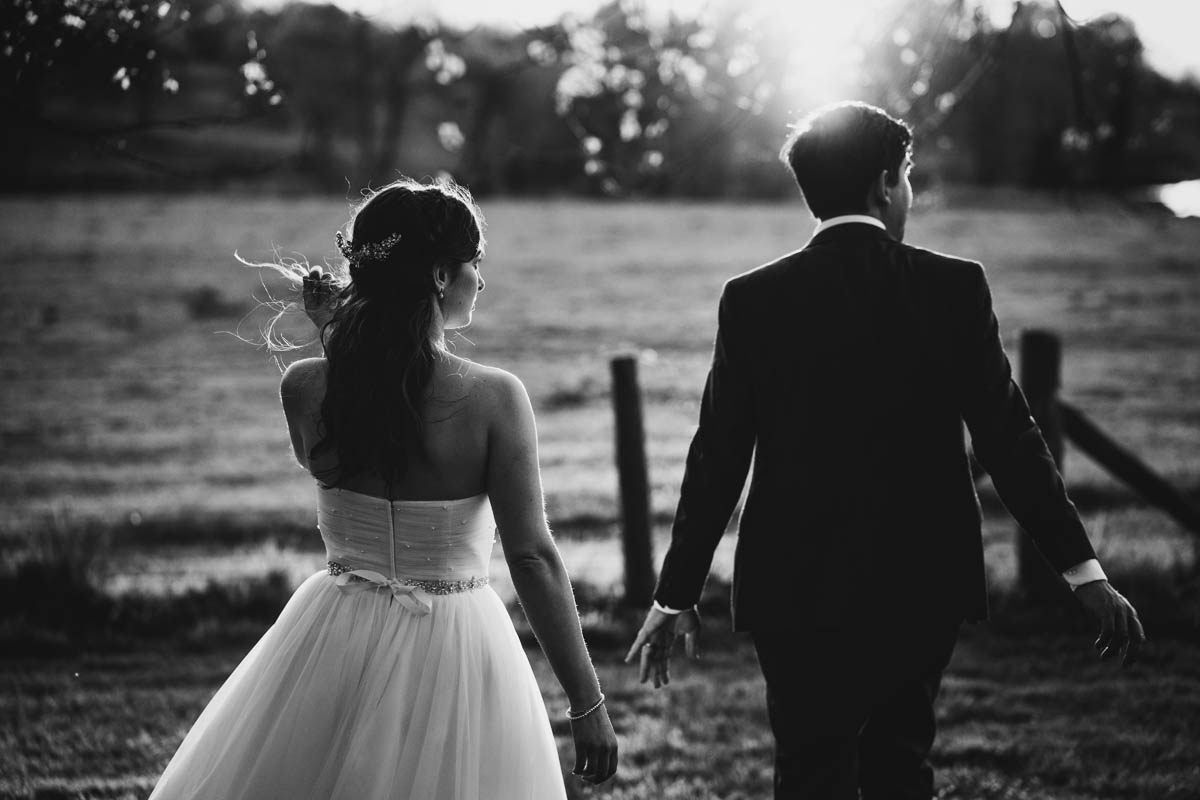 the bride and groom walk away from he camera. the bride flicks her hair and low golden sun hits them from behind