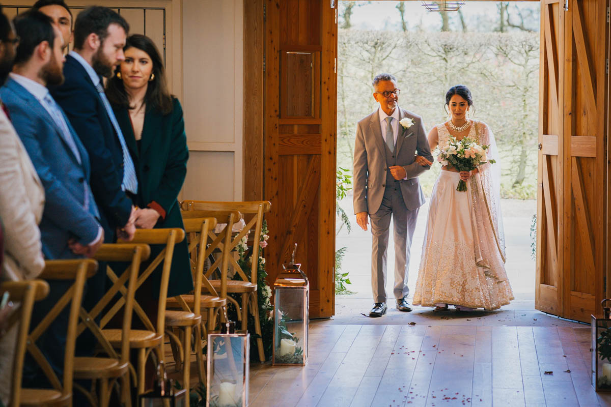 the father of the bride walks his daughter up the aisle while guests stand and watch