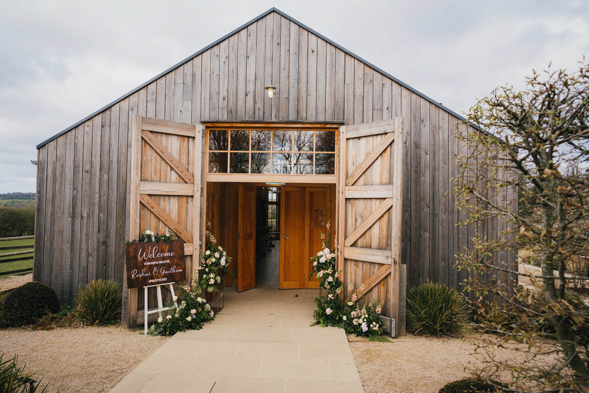the barn at Hyde house with wooden doors open and a floral arrangement with wedding sign outside