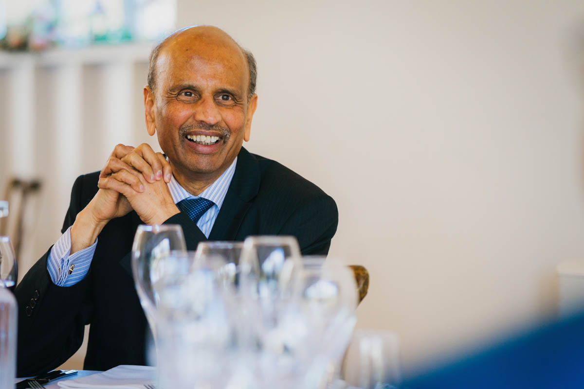 a male wedding guest laughs at the wedding speeches, empty wine glasses are out of focus in the foreground