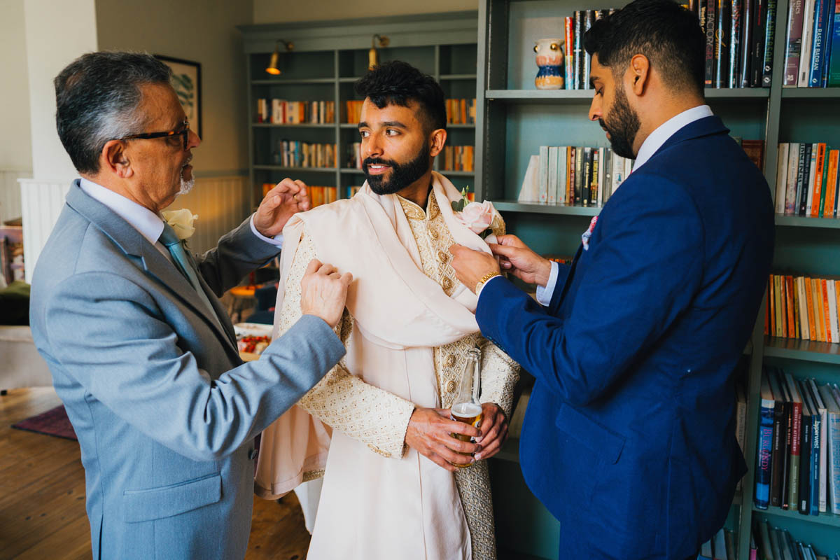 the groom's father and his friend assist him to dress for the wedding