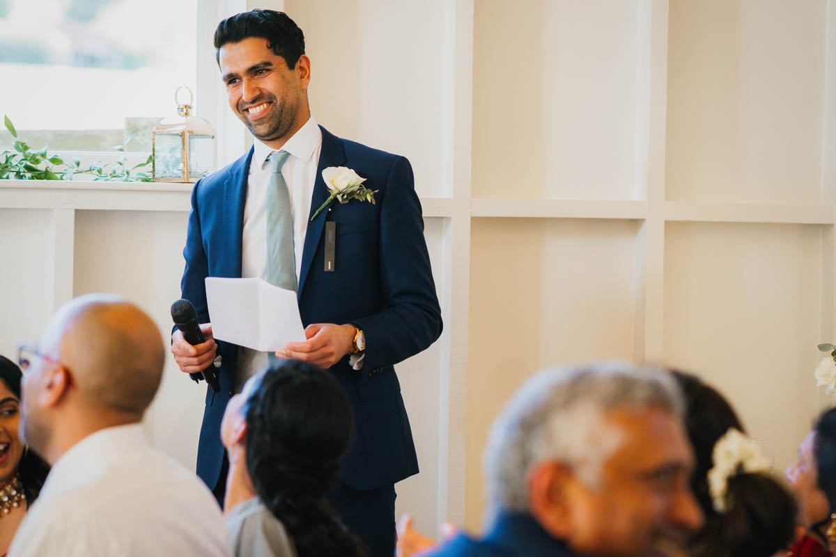 best man delivery his speech while out of focus wedding guests smile in the foreground