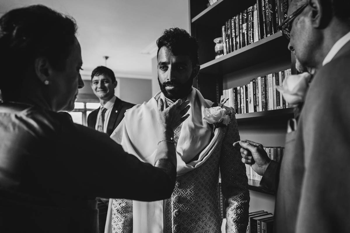 black and white photograph of the groom looking serious as wedding guests tidy up his buttonhole