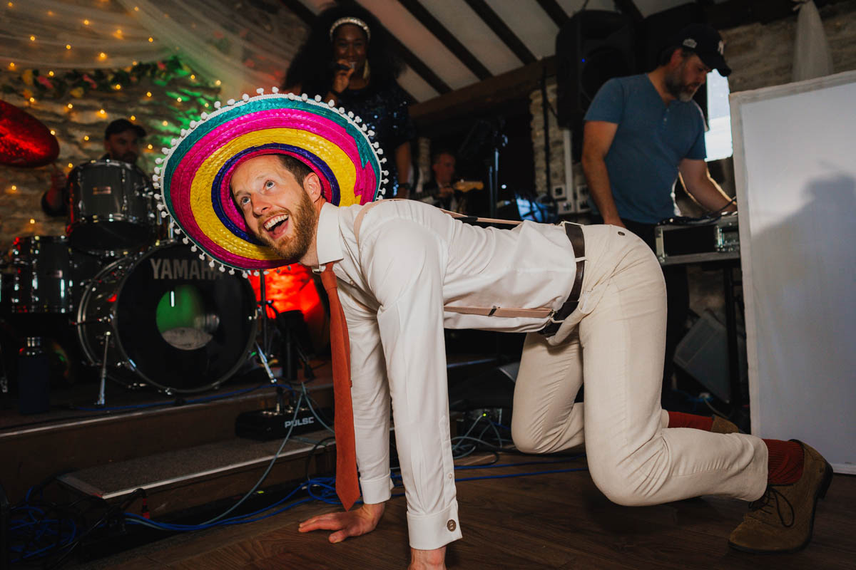 the groom dances on his hands and knees on the dance floor in a sombrero