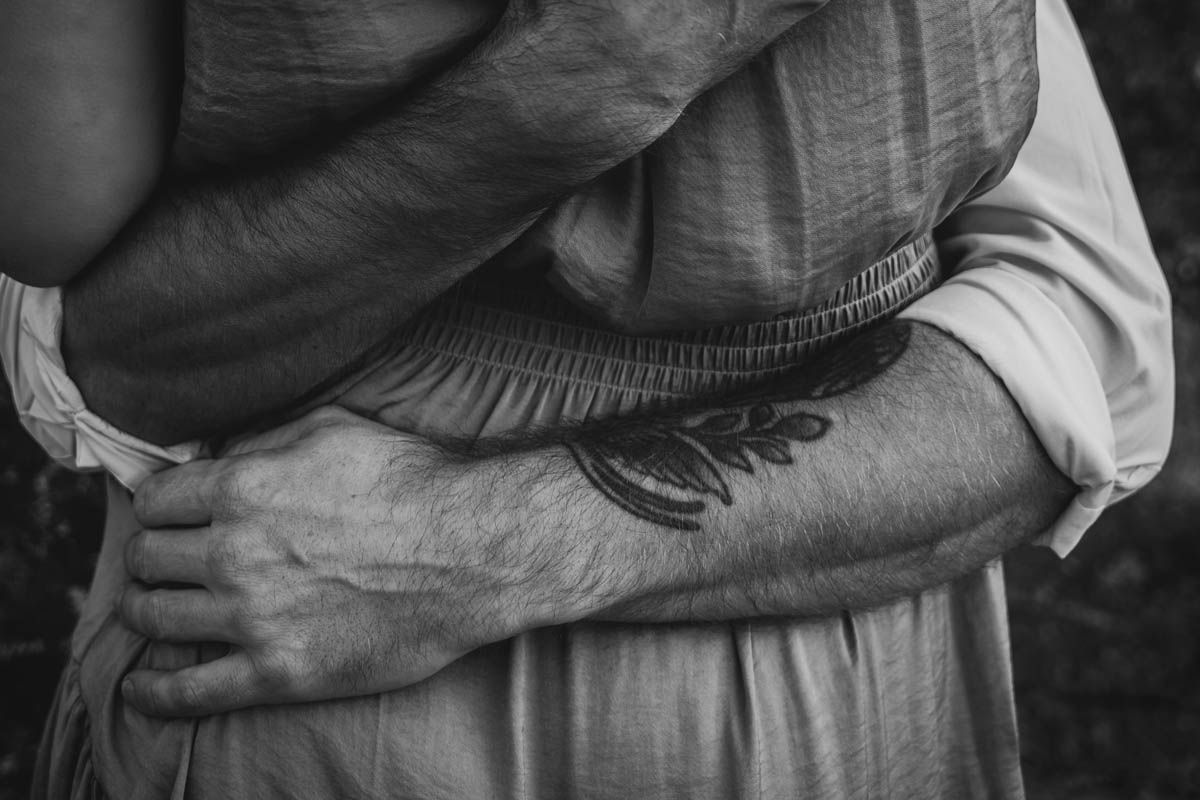 a close up monochrome photograph of a man's arms around his fiancé