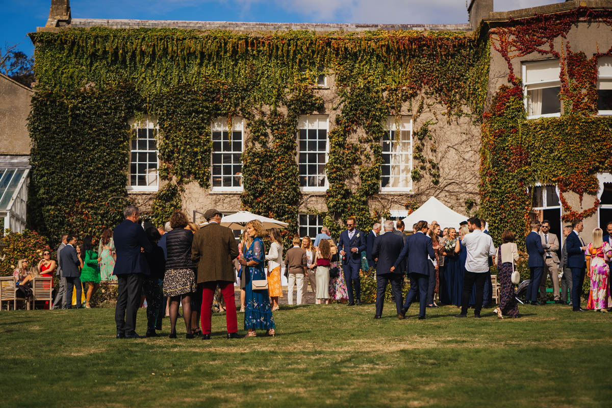 wedding guests during the drinks reception outside the front of pennard house which is covered in red and green ivy