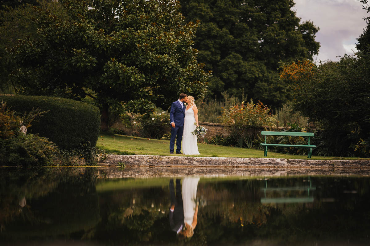 a newly married couple are reflected in the water of the lake at pennard house