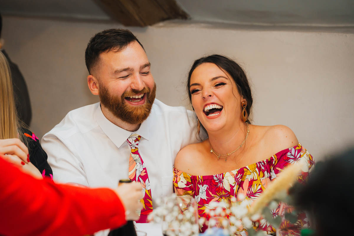 a couple laugh together whilst they eat their wedding breakfast