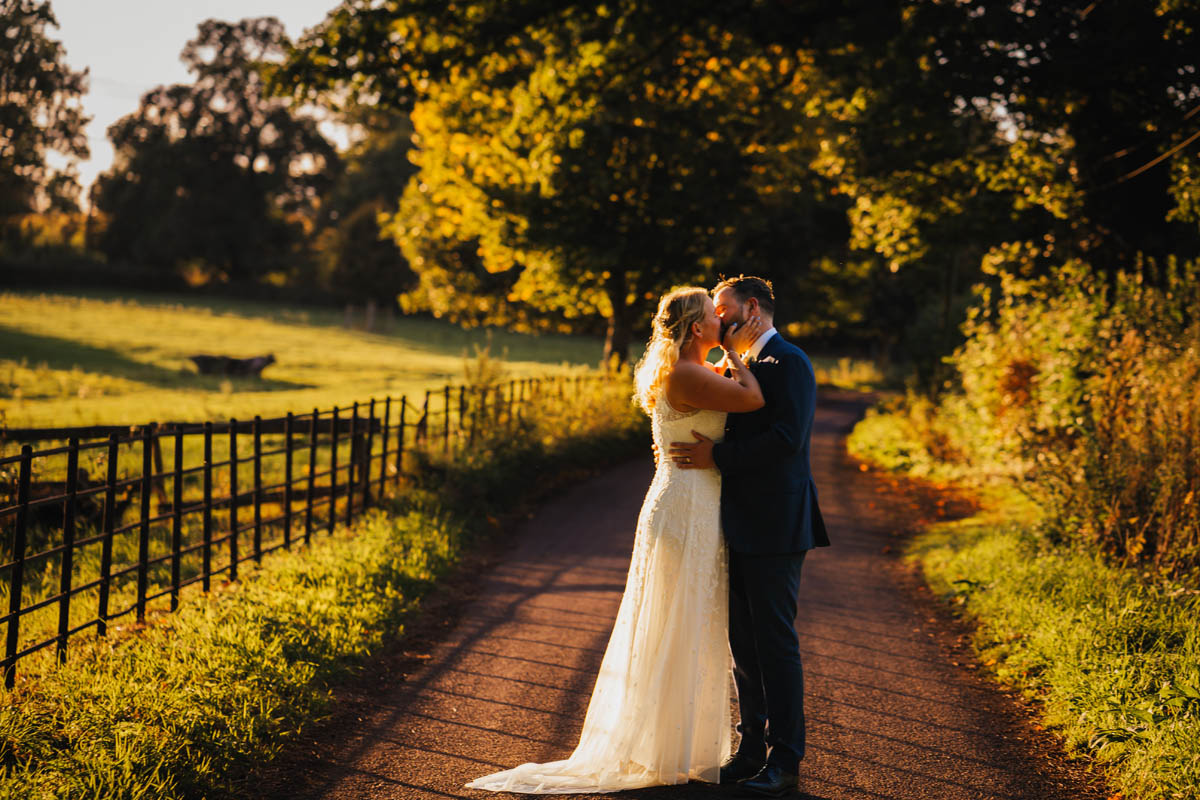 a couple kiss on a lane at golden hour in their wedding attire