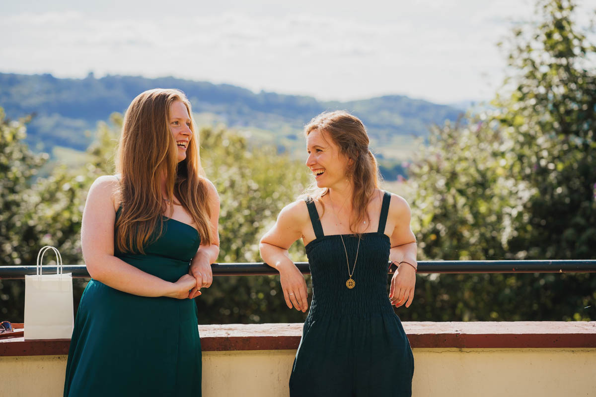 two wedding guests wearing green dresses laugh at one another