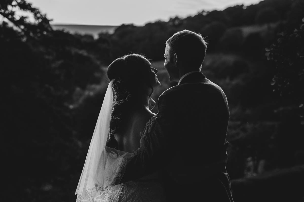 black and white silhouette bride a groom looking out over the Monmouthshire countryside. the light catches the bride's veil to create a beautiful highlight and the sun hits the couple from the front, creating a rim light