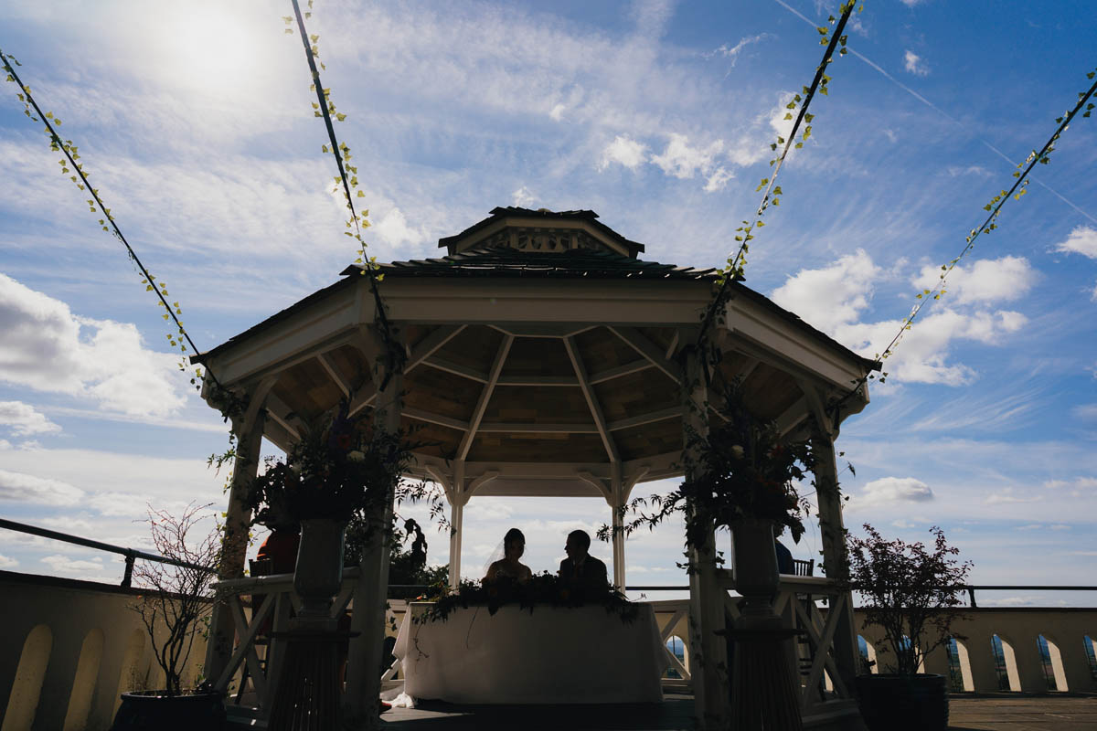 a silhouette of the bride and groom signing the register under the gazebo at caerllan. The Skye is blue and cloudy and the gazebo frames the newly-weds