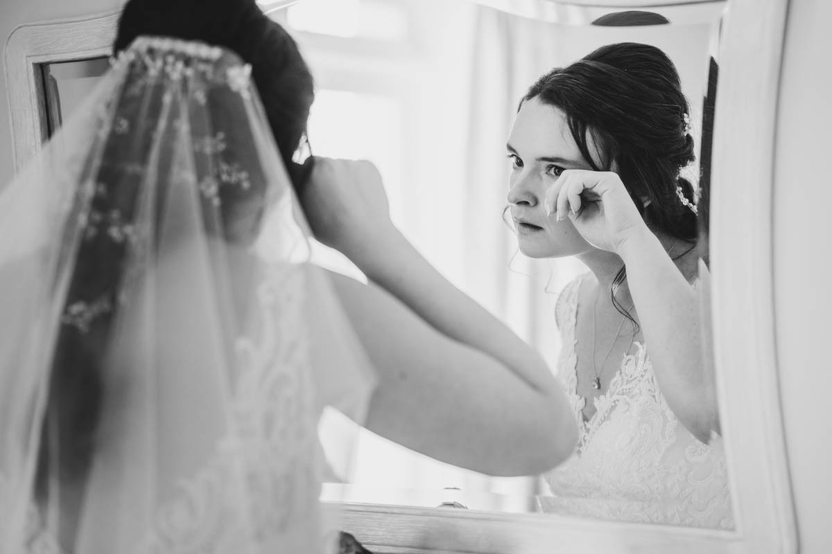 the bride wipes away a tear using a mirror to check her reflection. Monochrome photograph