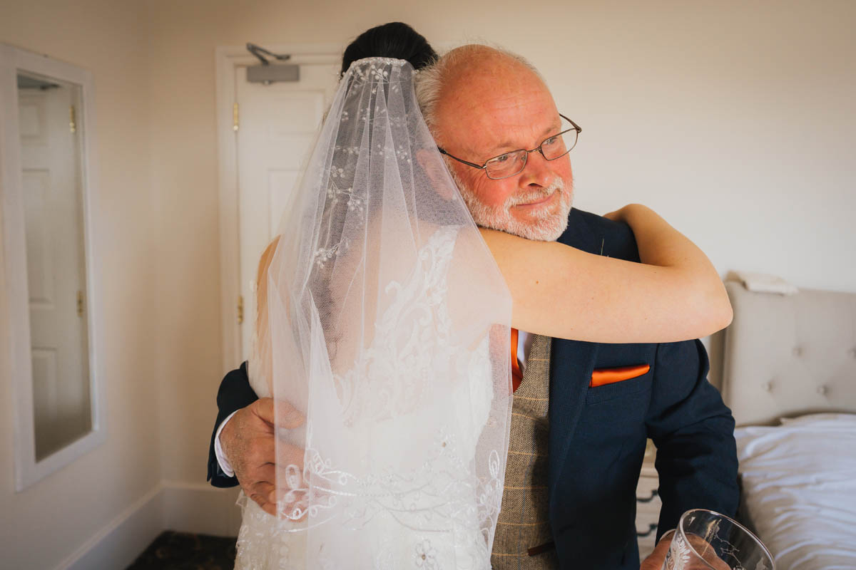 the father of the bride embraces his daughter as he sees her in her dress for the first time