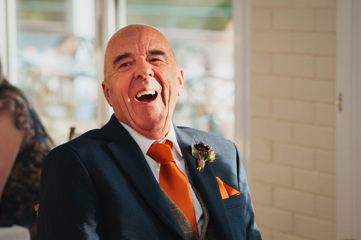 the father of the groom throws his head back as he laughs at the wedding speech