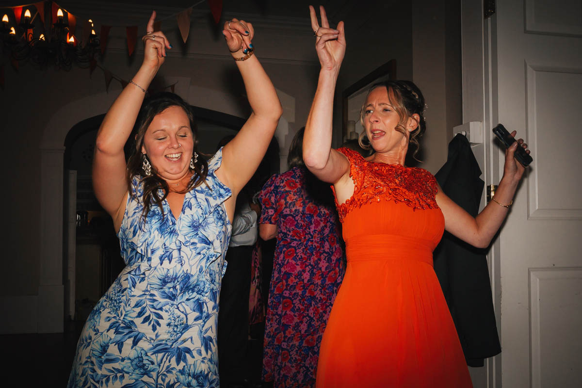 a bridesmaid and wedding guest throw their arms in the air as they party