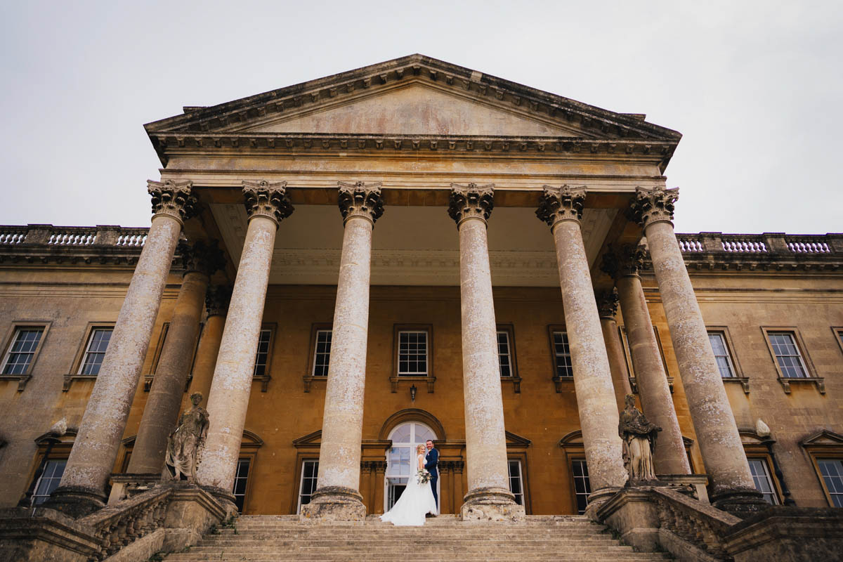 The front of Prior Park Mansion with the corinthian columns and a bride and groom in the middle