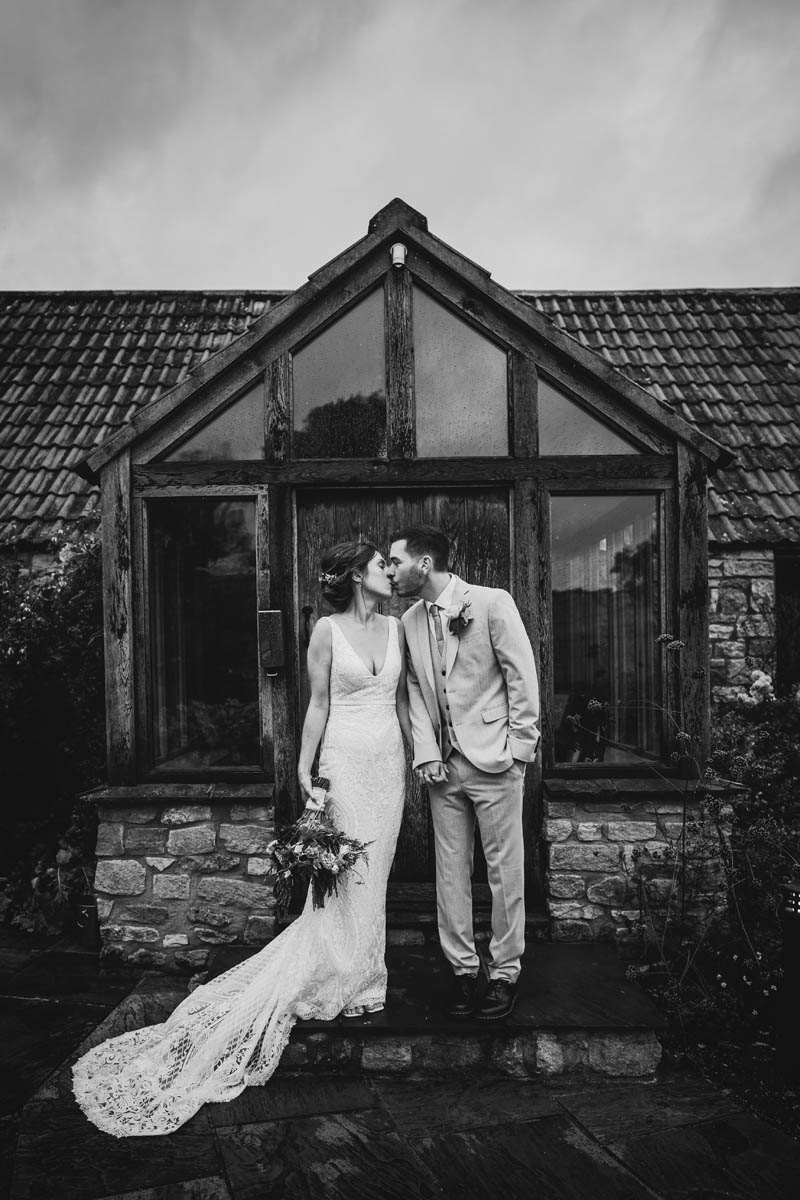 black and white photograph of the newly weds kissing outside priston mill tythe barn