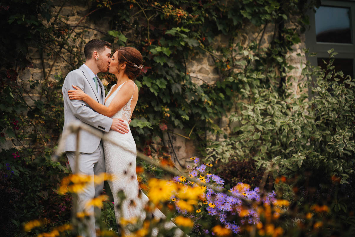 the bride and groom kiss surrounded by flowers at the the barn