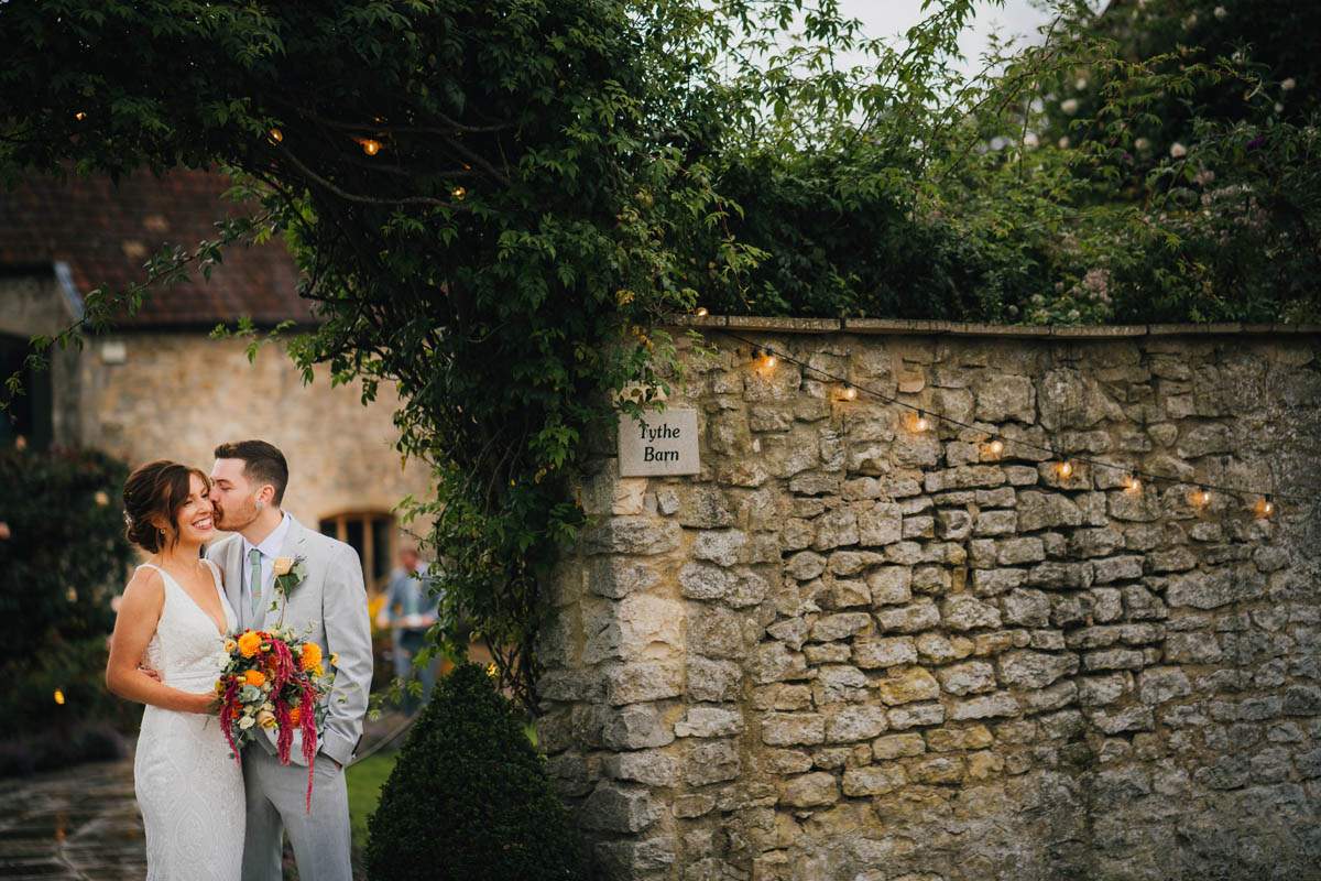 the groom kisses his bride under the archway at the the barn in priston