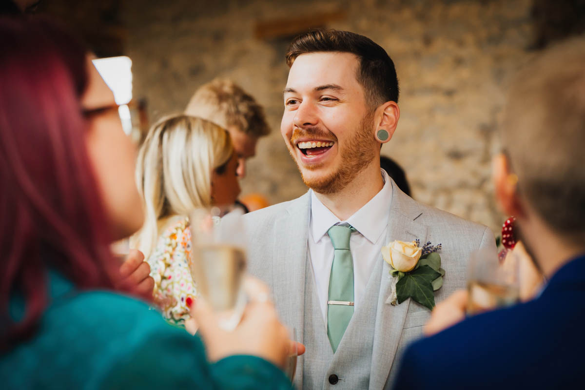 the groom laughs as he talks to wedding guests
