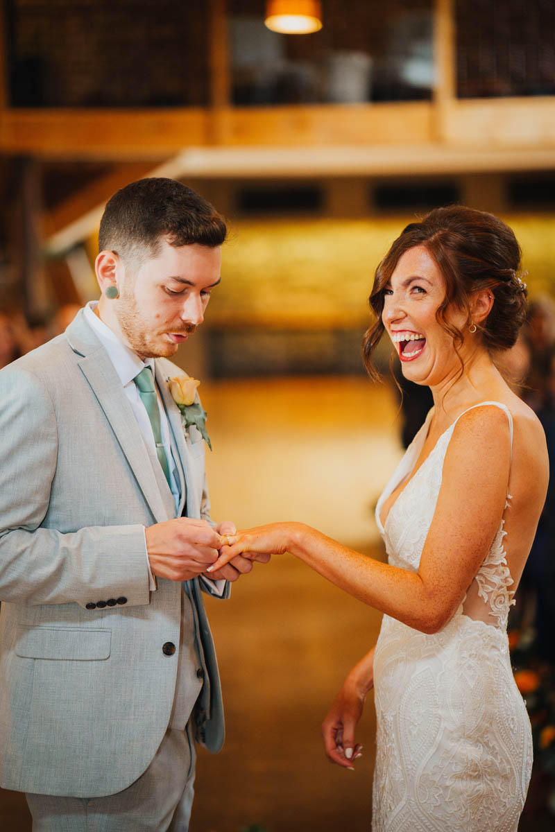 the bride laughs as the groom struggles to get her wedding ring on her finger