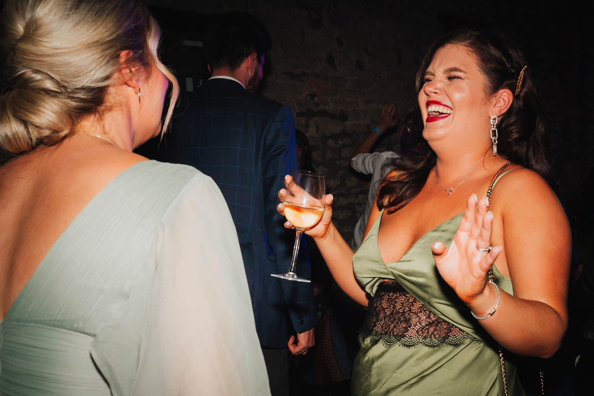 a wedding guest dances as she drinks a glass of wine
