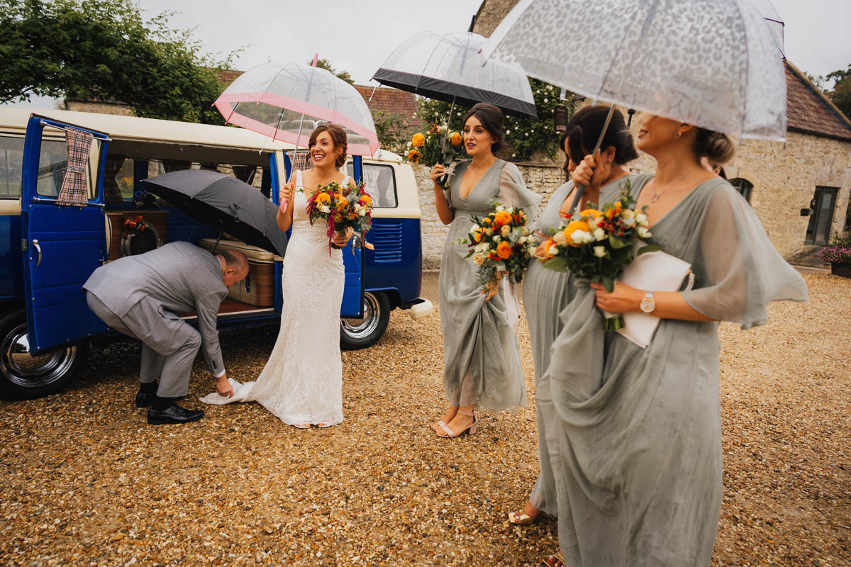 the bride and her bridesmaids holding umbrellas as they get out of the blue VW camper van
