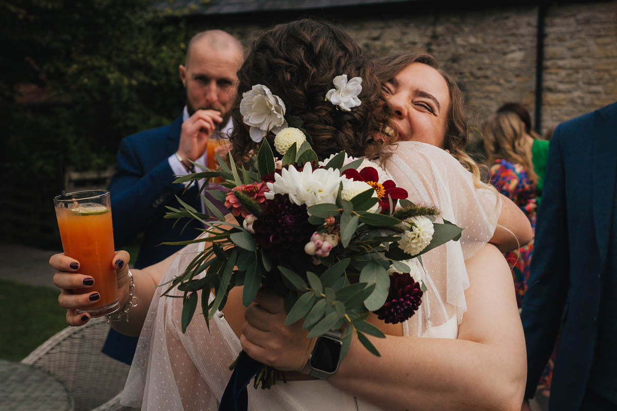a bridesmaid holding a bouquet hugs the bride