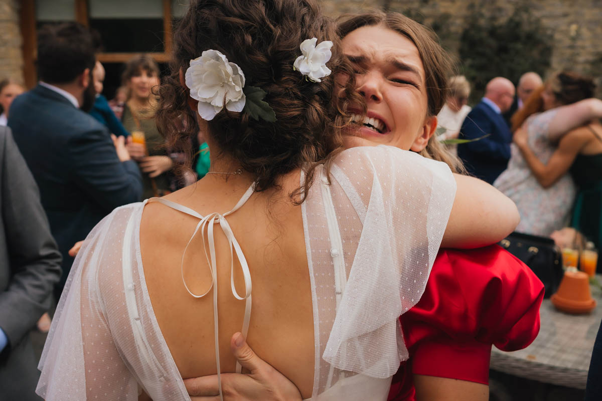 a woman in a red dress hugs the bride as she cries