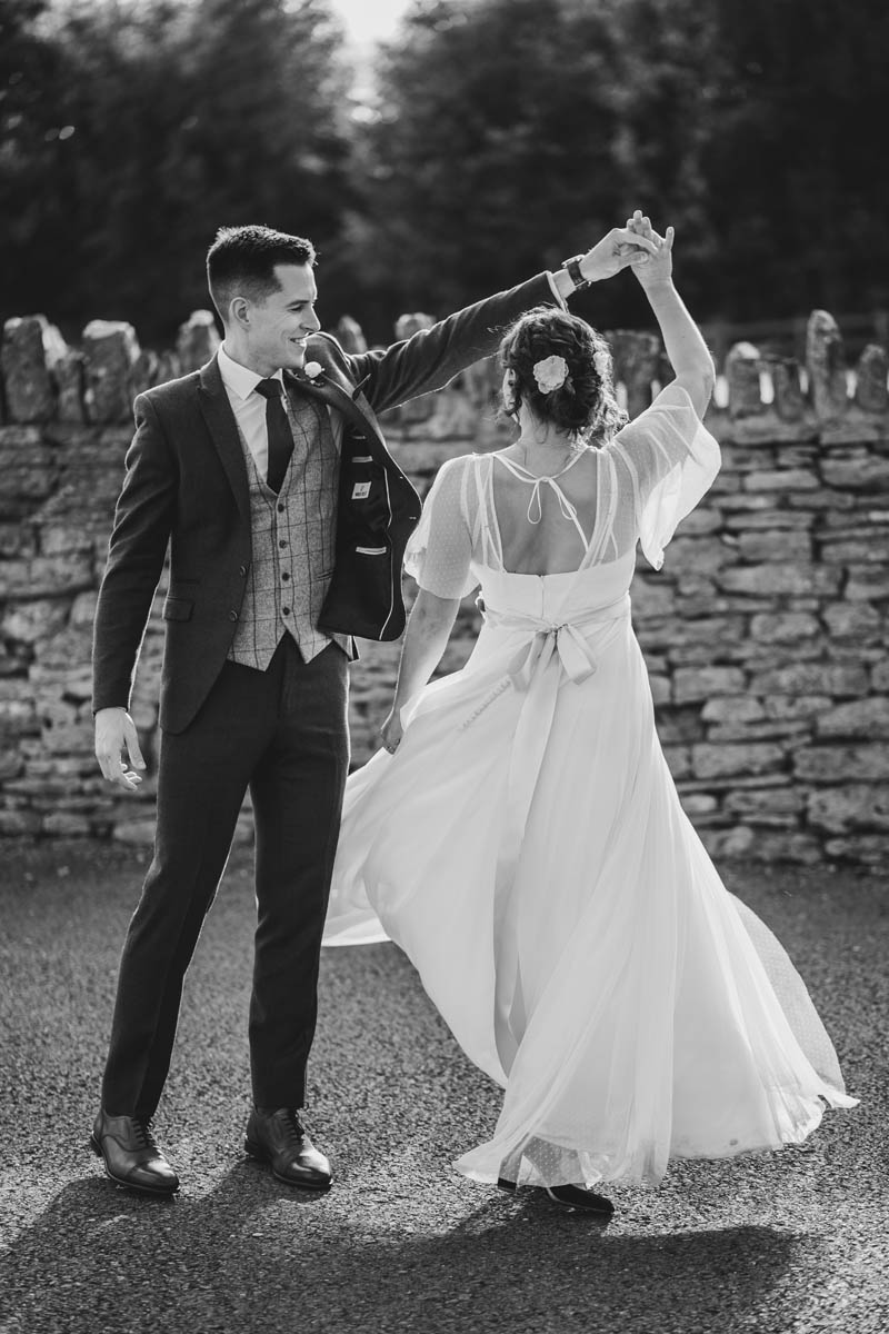 black and white photograph of the groom spinning his bride around, her a-line dress flows as she spins