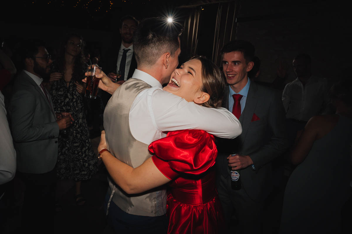 a woman hugs her brother on the dance floor. Off-camera flash fires creating a starburst in the distance behind