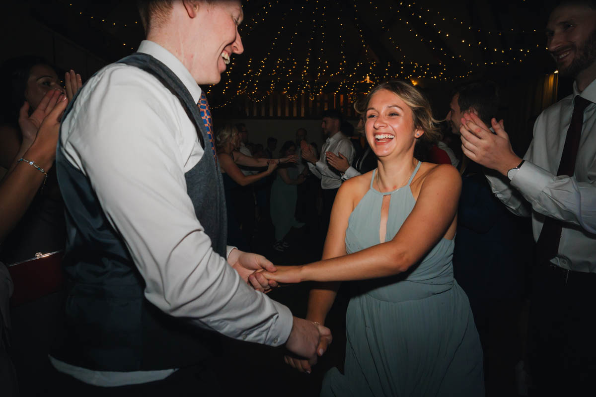 a bridesmaid holds her partners hands as they dance, fairy lights create bokeh in the background