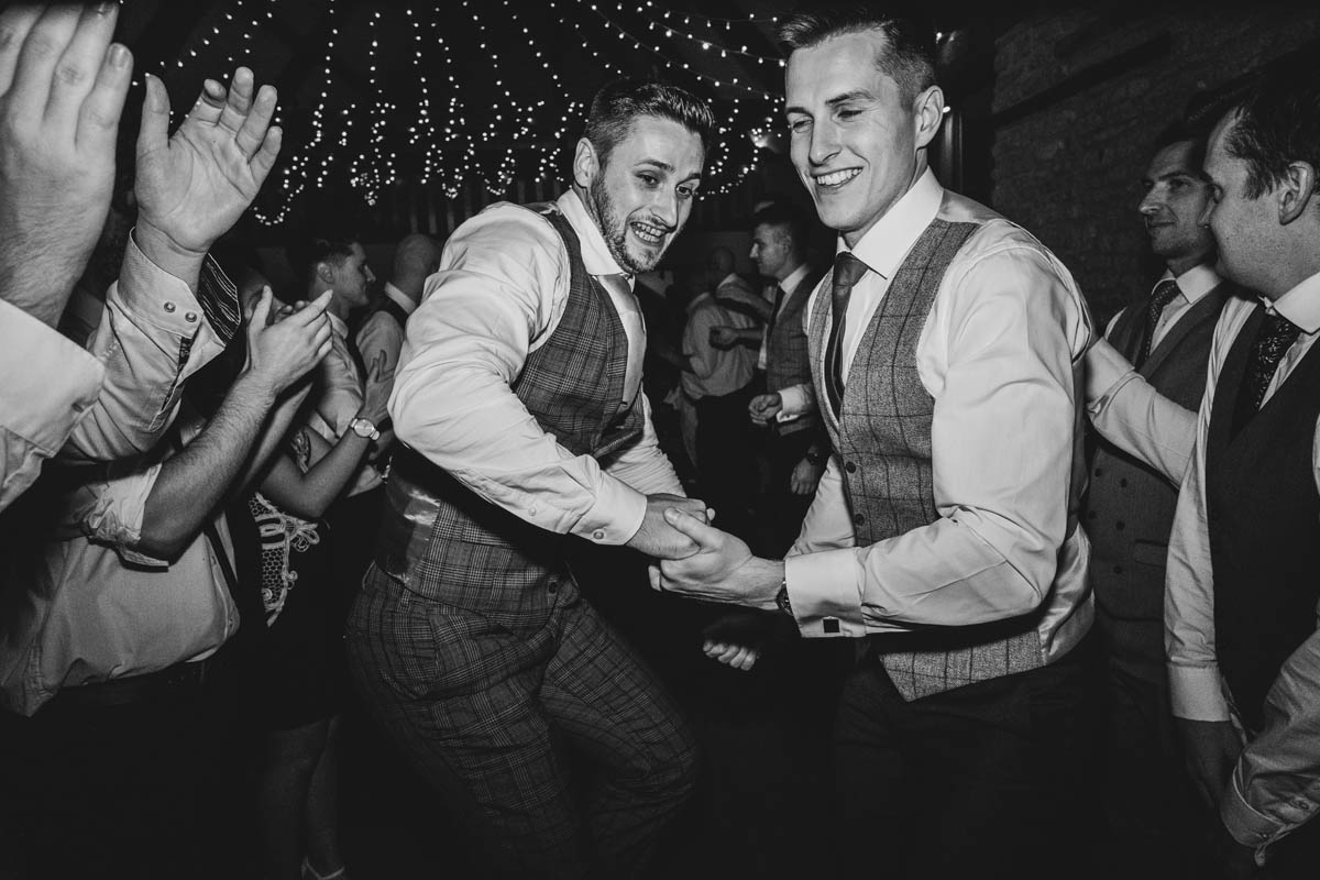 black and white photograph of two men holding hands as they dance at a wedding