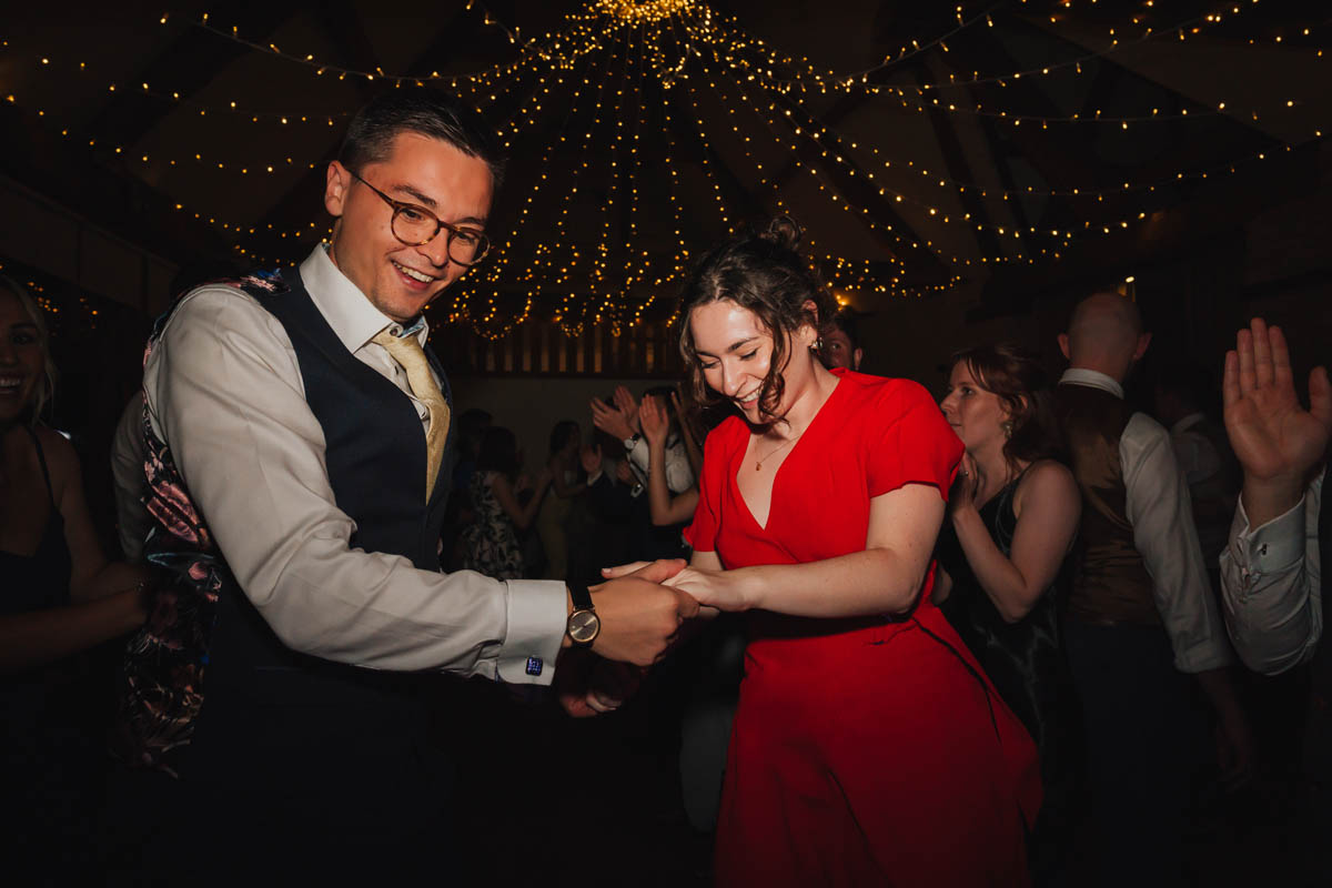 a woman in a red dress and a man in a suit dance a ceilidh at a wedding