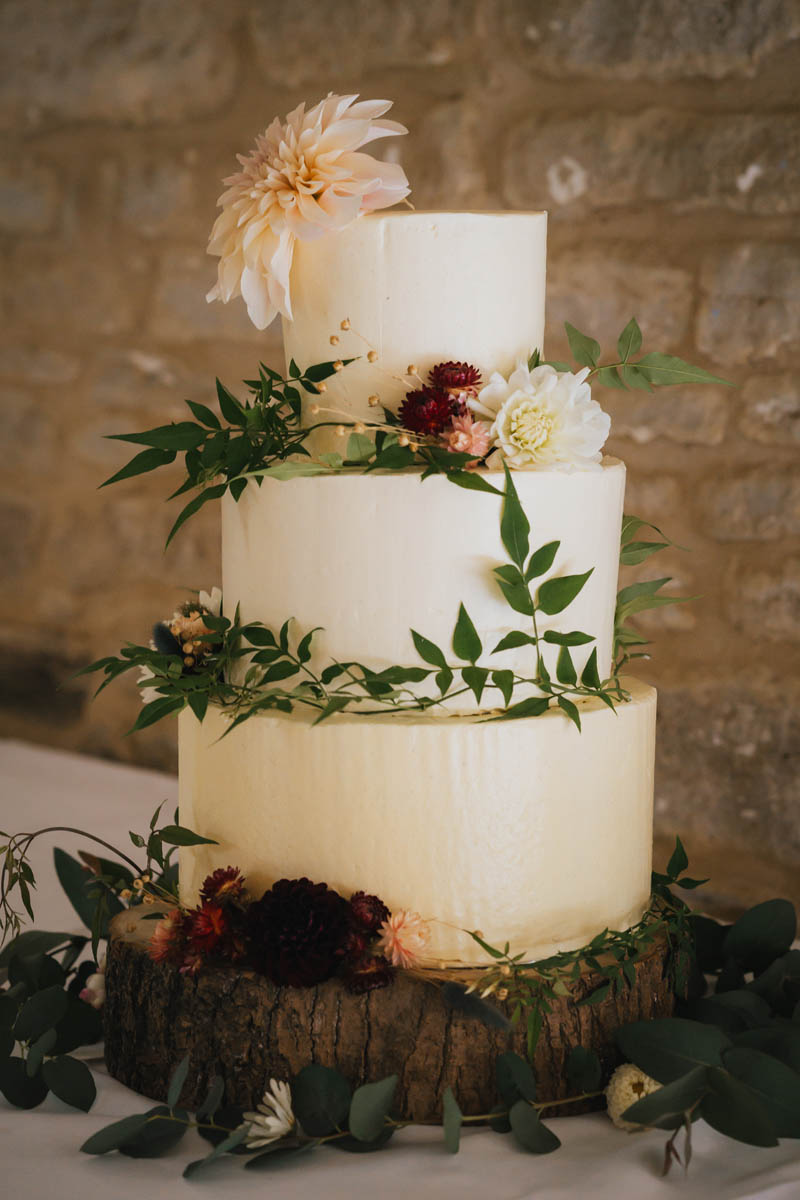 a three-tiered wedding cake with green foliage and dark burgundy flowers
