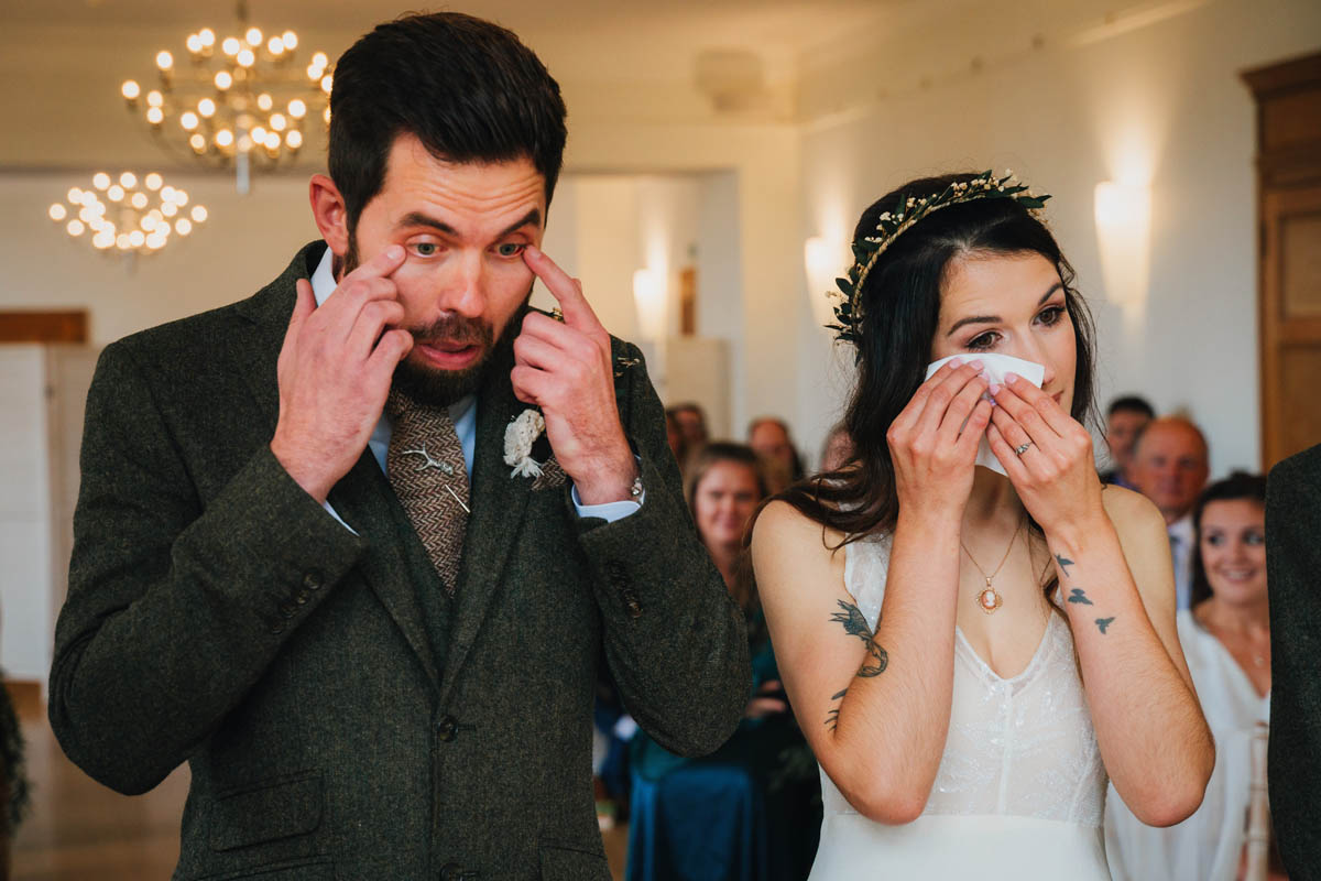 both bride and groom wipe away tears during their wedding ceremony