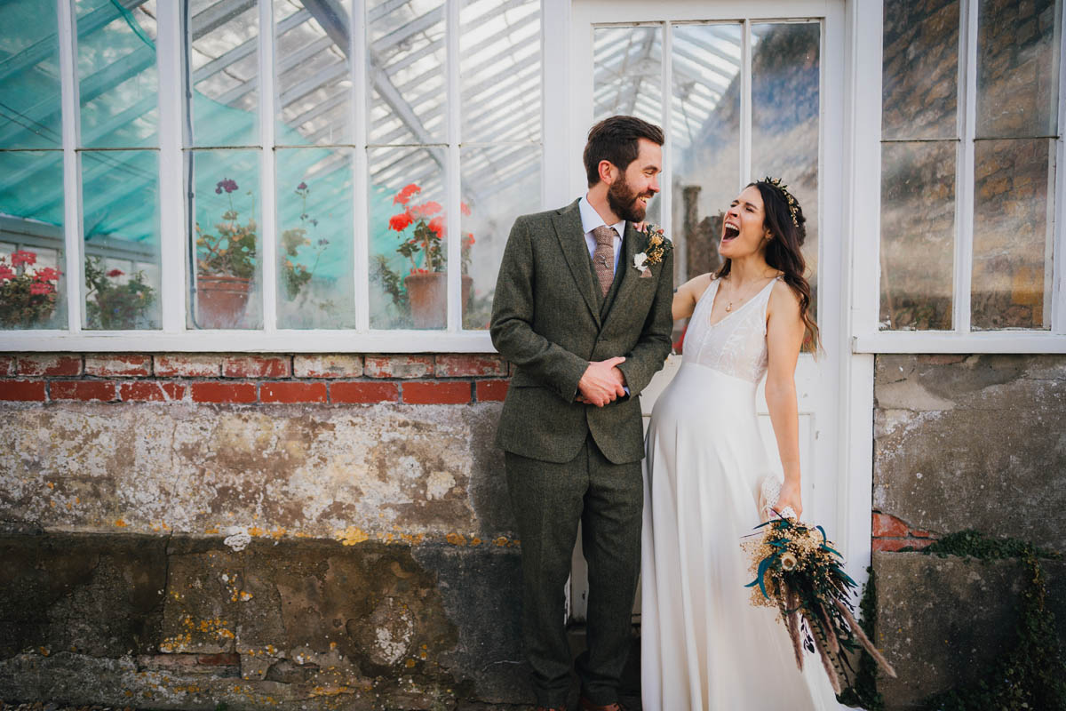 the bride laughs at her groom in front of the greenhouse at Coombe Lodge