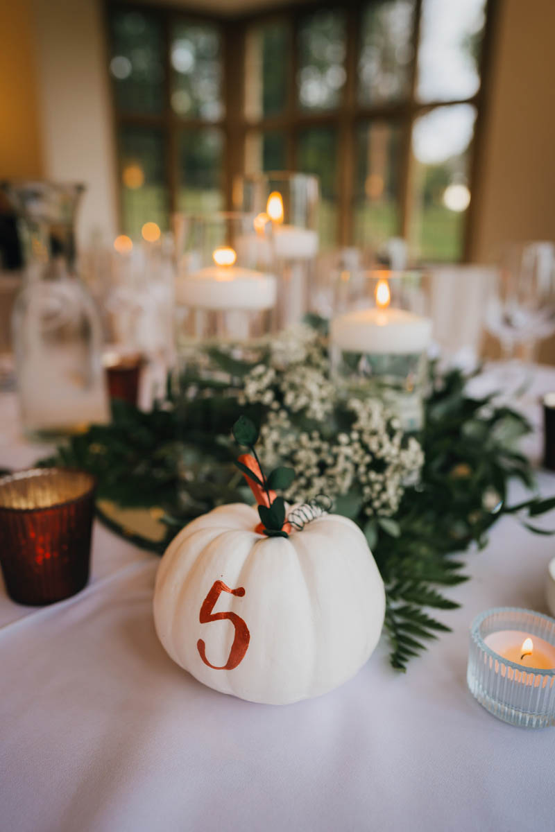 a pumpkin table number with candles and ferns behind
