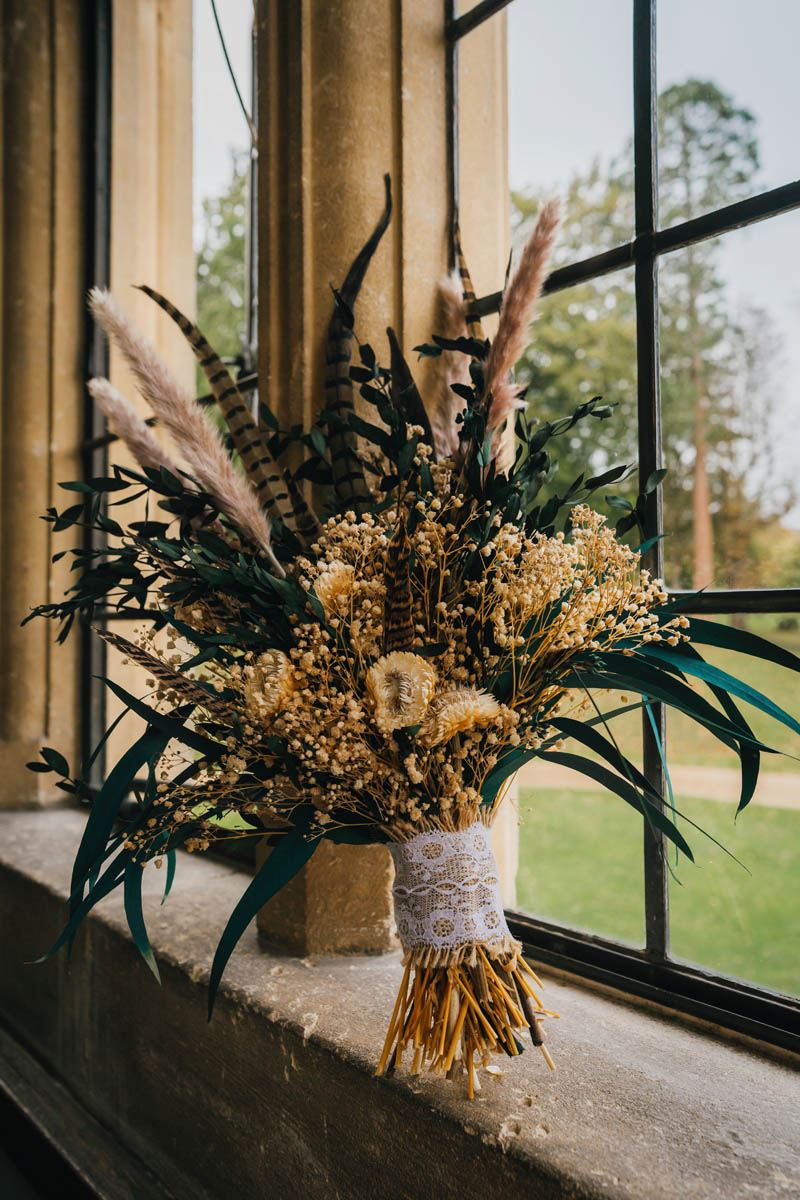 the bridal bouquet, dried flowers with green foliage and peacock feathers with lace ribbon tied around the stems