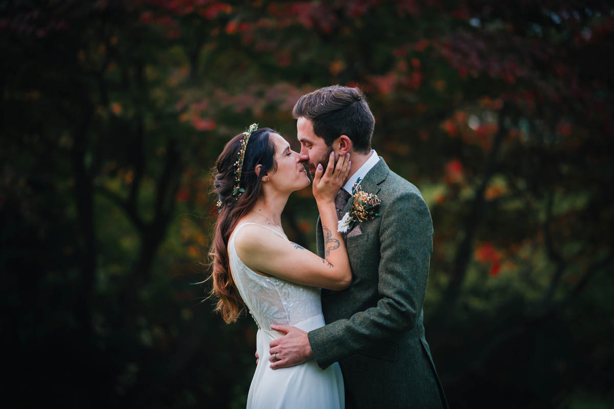 the bride brings her husband in for a kiss in front of a red acer behind