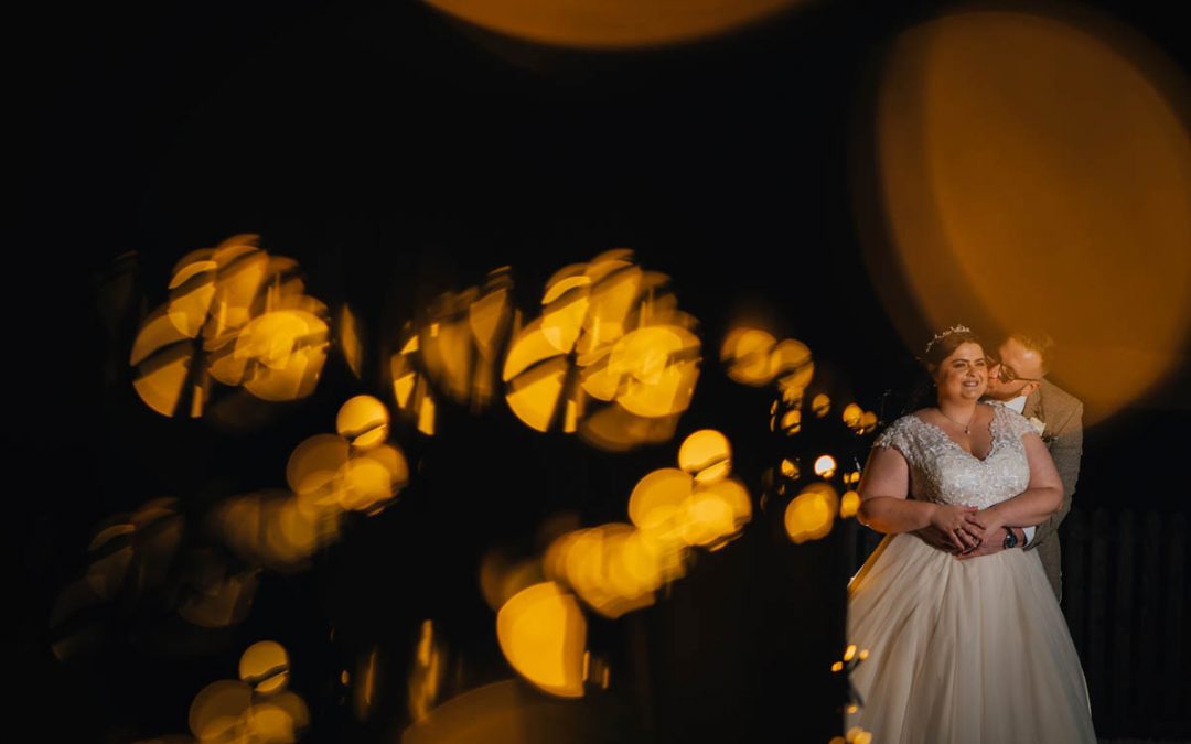 fairy lights create bokeh and the bride and groom post towards the back of the image, they are lit by an off camera flash